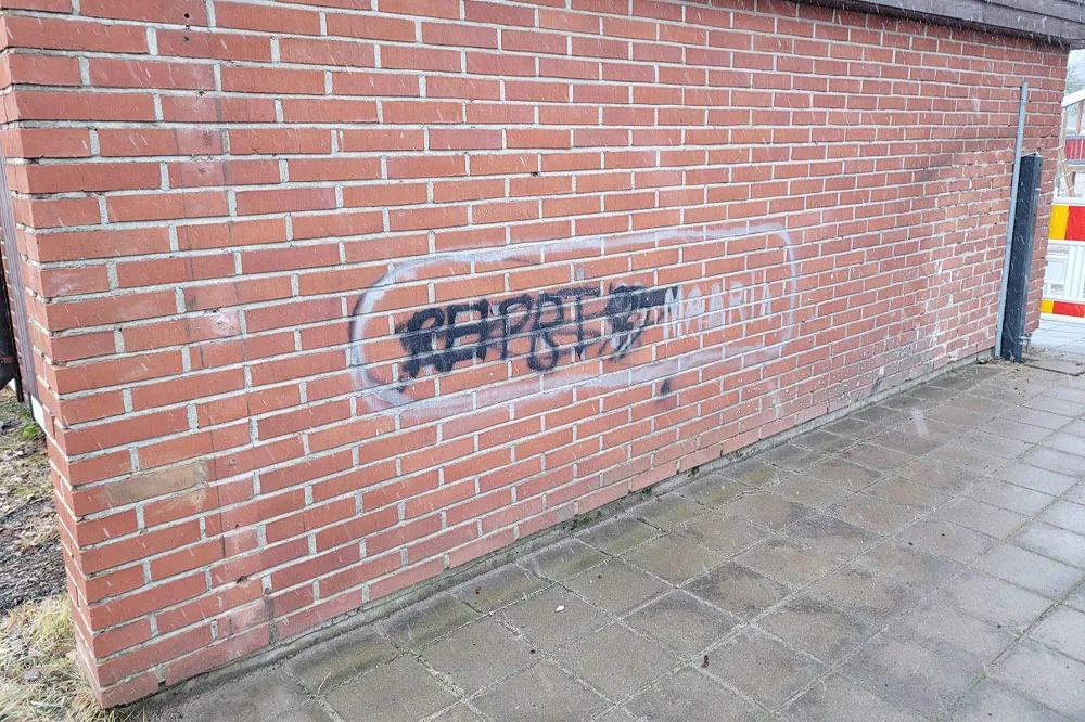 Mustalla ja valkoisella spraymaalilla maalattu graffiti punaisessa tiiliseinässä